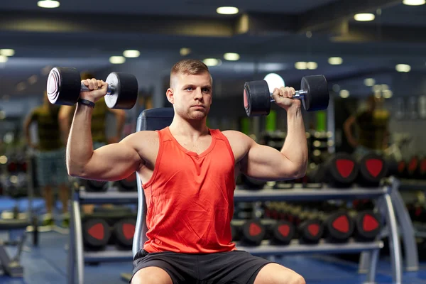 Молодой человек с гантелями, разминая мышцы в тренажерном зале — стоковое фото